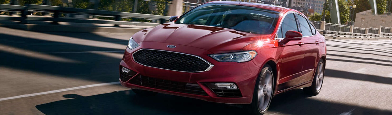 Red Ford sedan driving over a bridge on a sunny day.