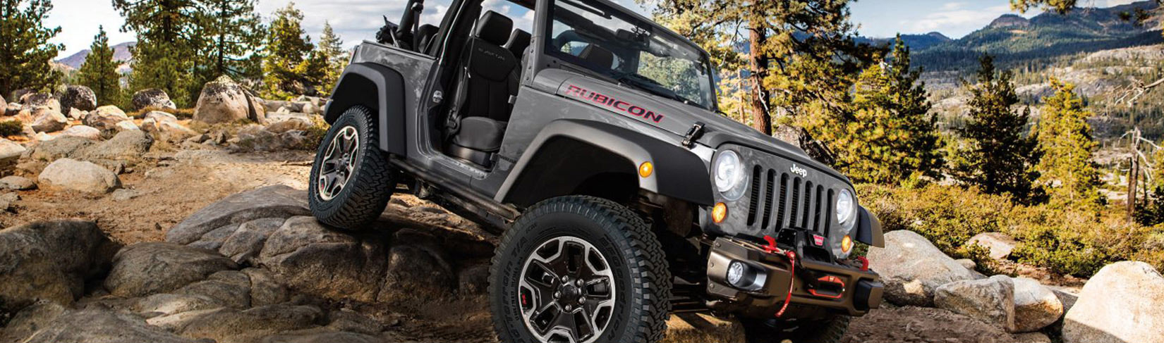 Gunmetal gray Jeep driving over rugged, mountainous terrain.