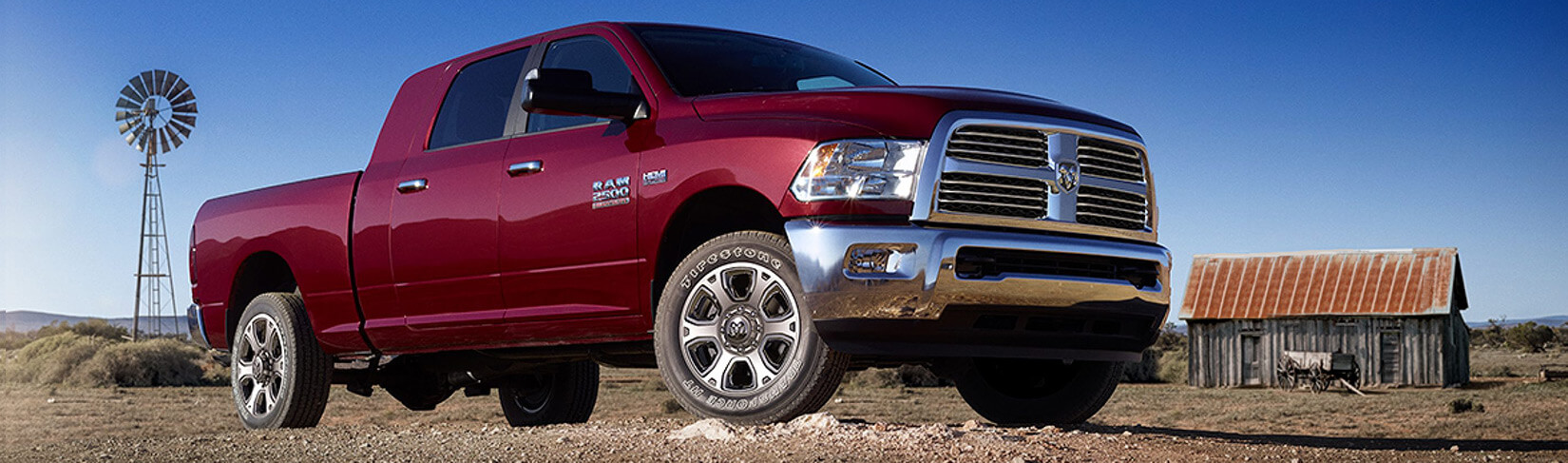 Maroon Ram pickup truck parked between a barn and a windmill.